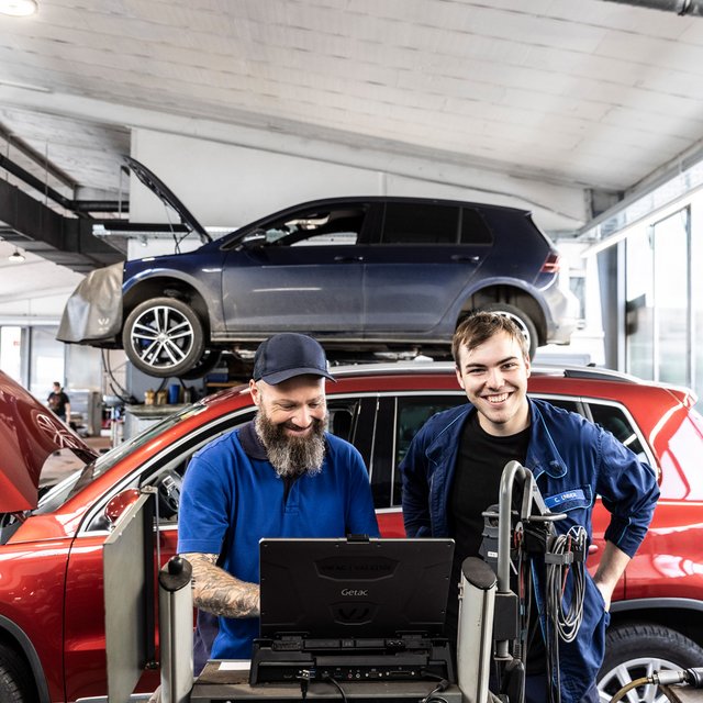 Zwei Werkstattmitarbeiter von Autohaus Biggel stehen vor einem roten Auto