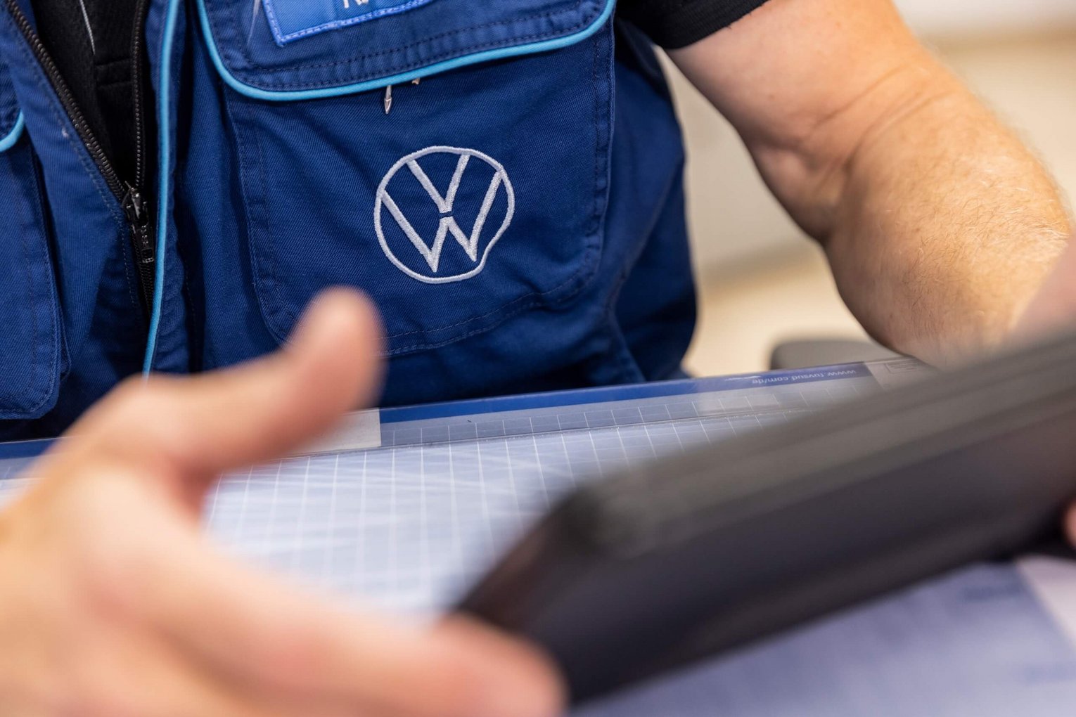 Nahaufnahme eines Mitarbeiters im Autohaus Biggel mit blauer Volkswagen-Weste, der an einem Schreibtisch arbeitet und ein Tablet in der Hand hält.